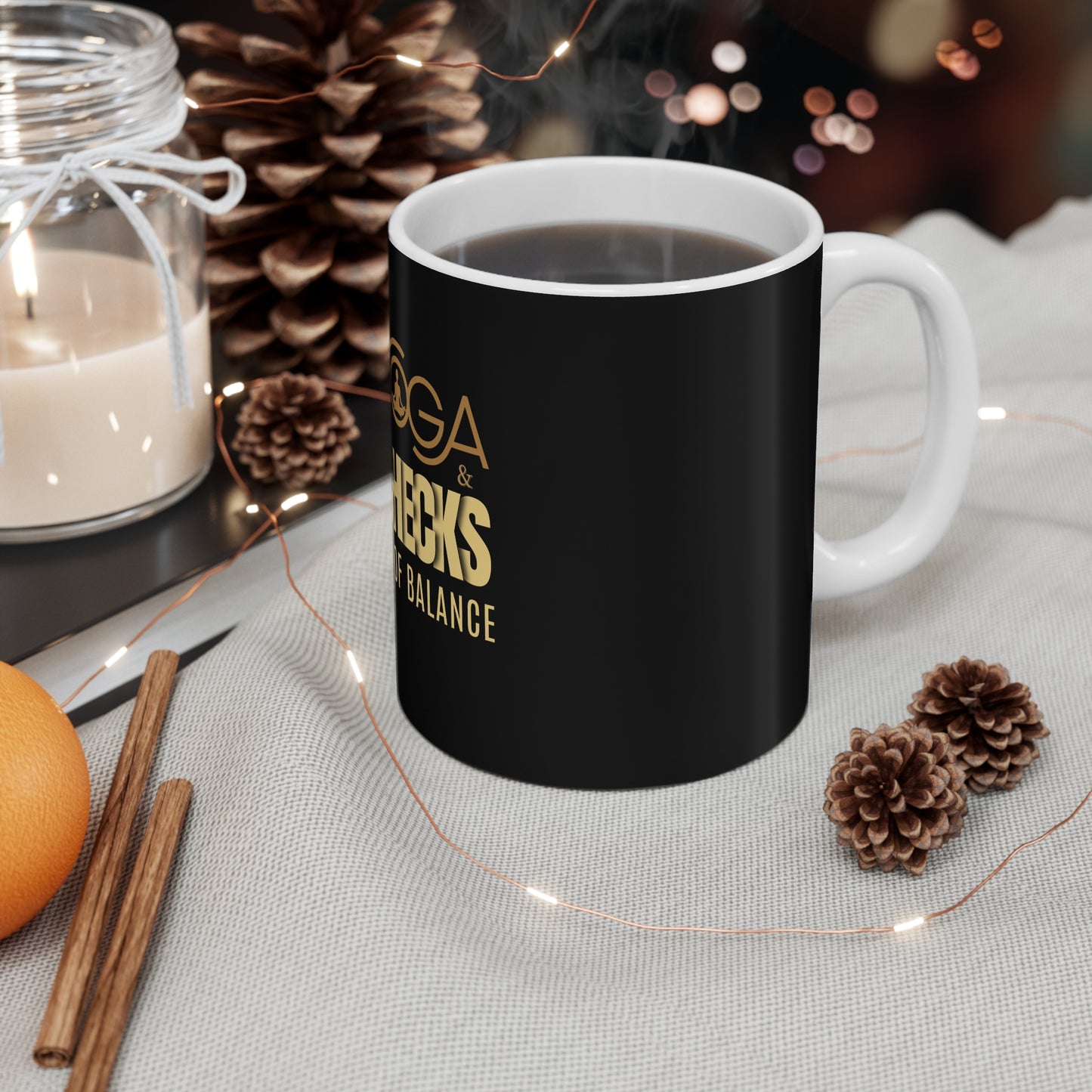 Black mug with text 'Yoga & Paychecks – My Kind of Balance' on a table with decorative items