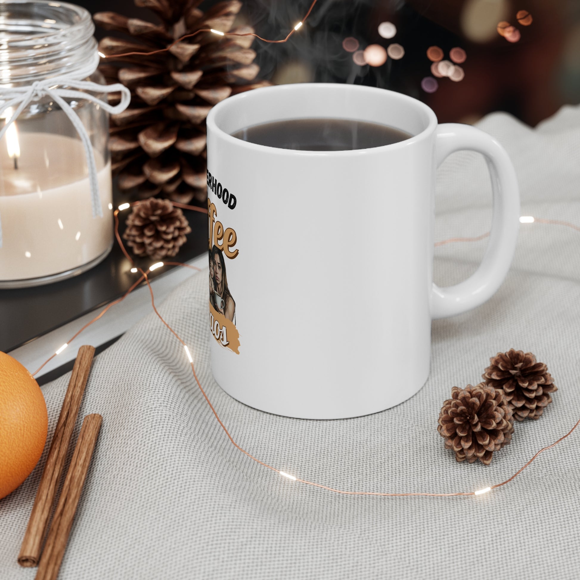 White mug with a coffee label on a table with decorative elements like a candle, cinnamon sticks, and pine cones.