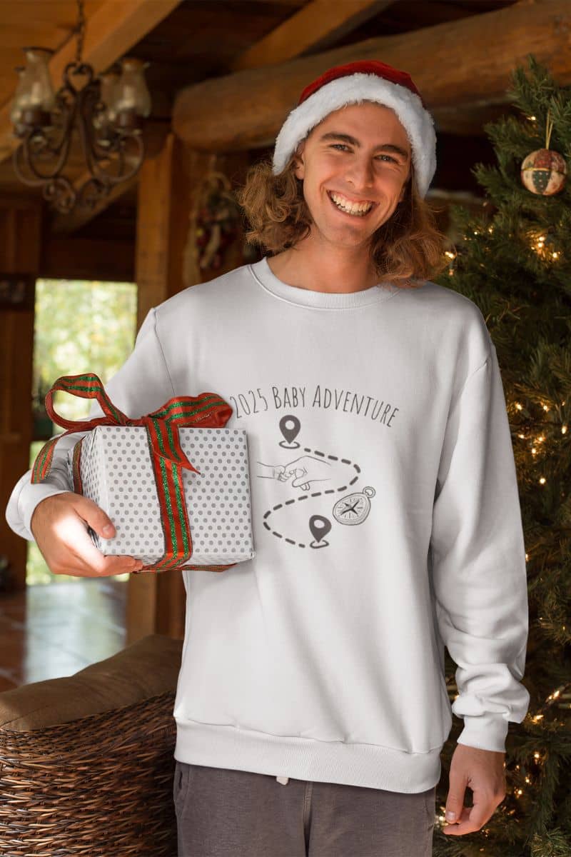 2025 Baby adventure sweatshirt with a guy standing next to the Christmas tree while holding his gift