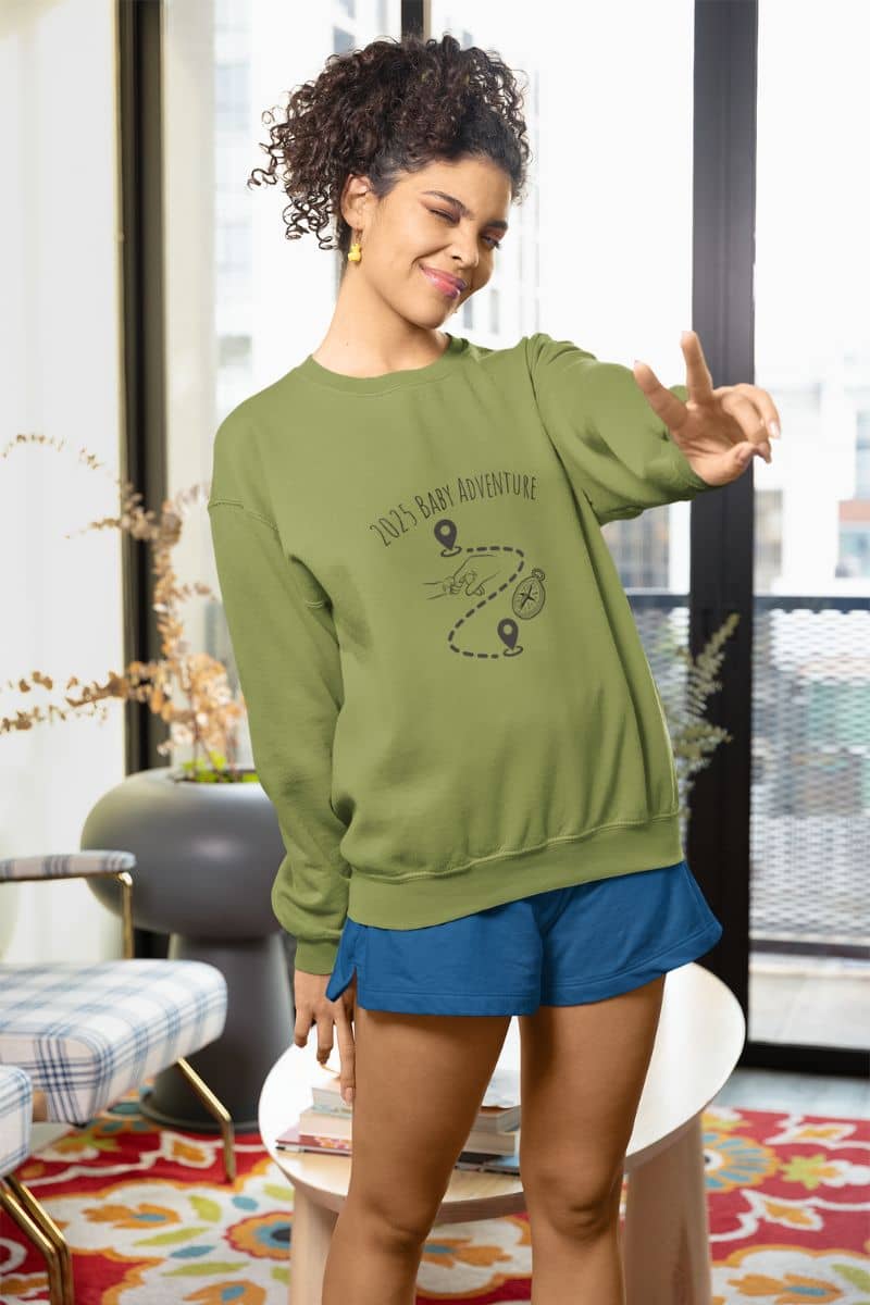 2025 Baby adventure sweatshirt with a girl standing and posing indoors with two fingers up and one eye closed