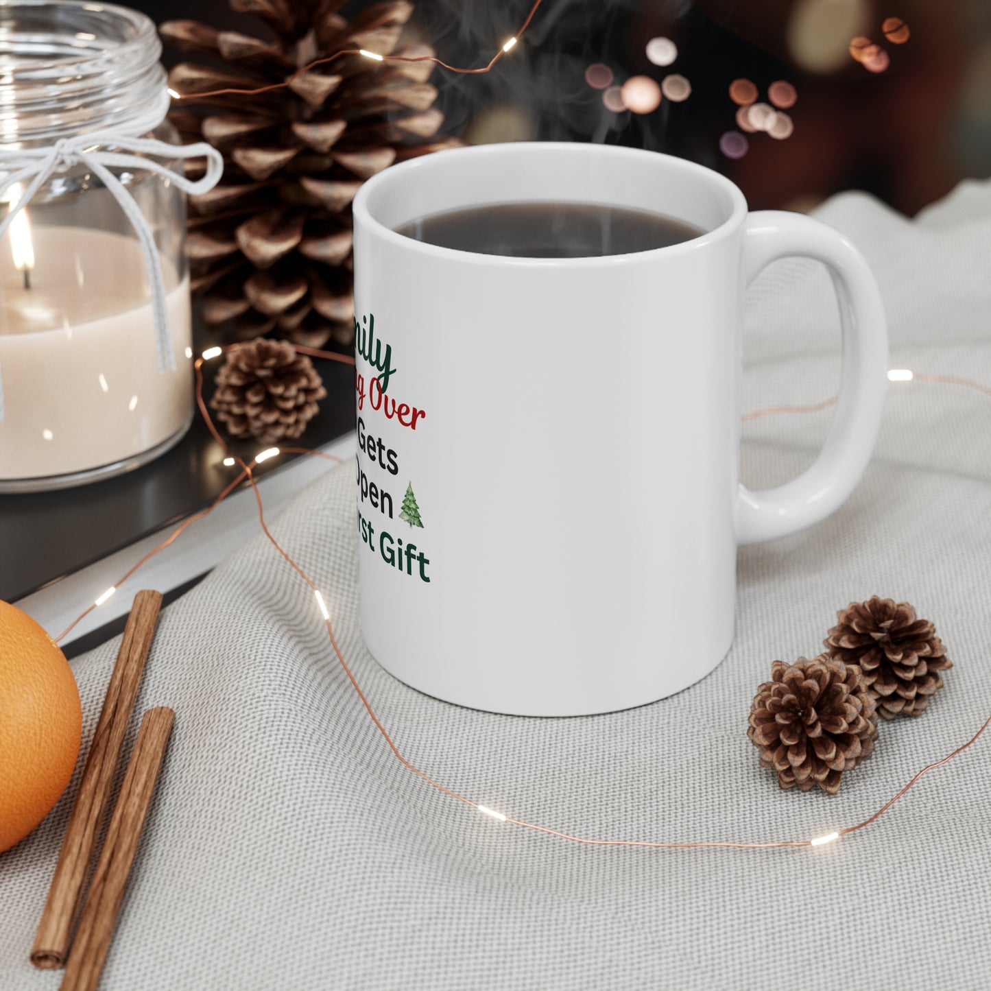 White mug with text 'Family: Arguing Over Who Gets To Open The First Gift', candle, cinnamon sticks, and pine cones on a table.
