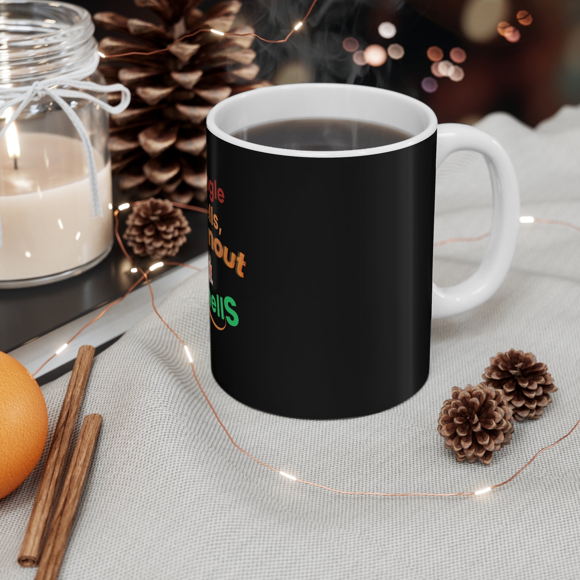 Black mug with colorful text 'Jingle Bells, Burnout Smells' on a table with decorative items