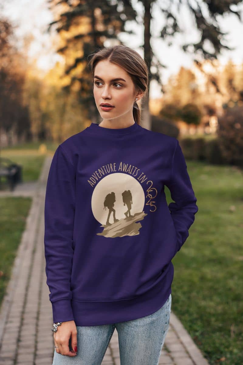 Adventure awaits in 2025 sweatshirt with the girl standing with her hands on her hips in the garden and looking to one side