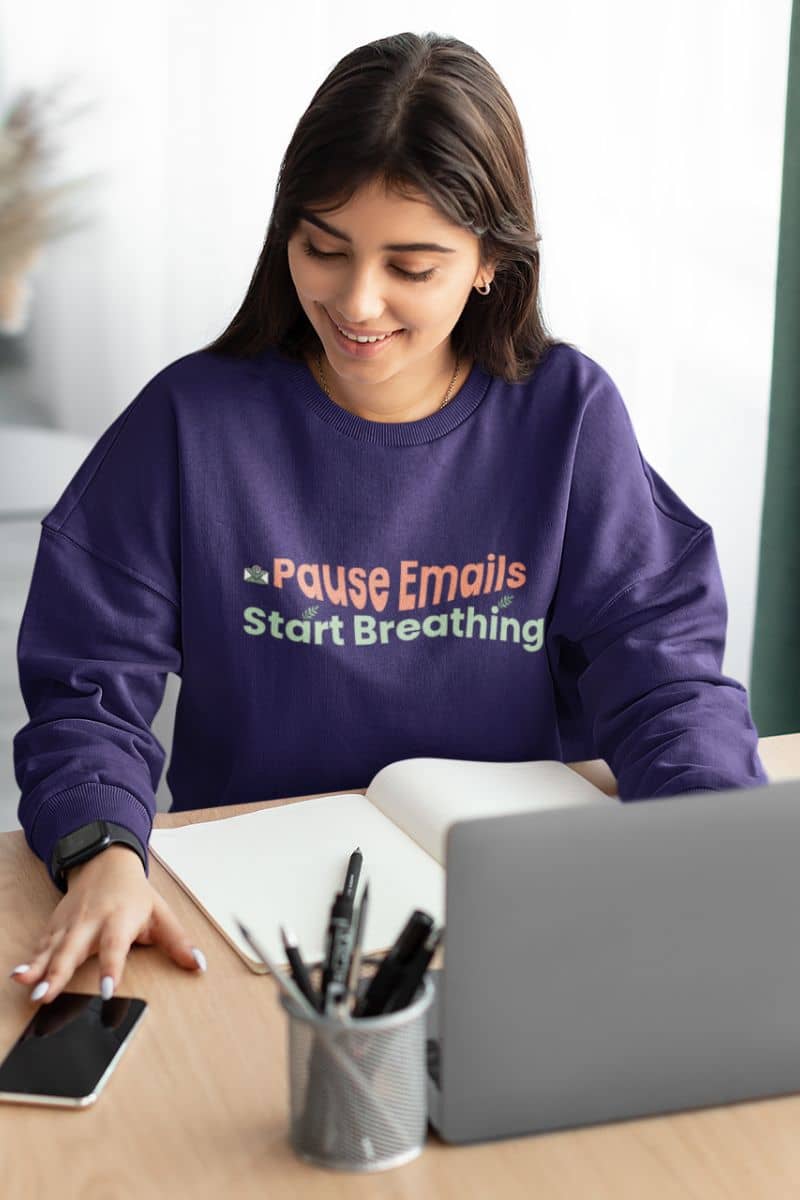 Anxiety relief pullover with a person wearing a purple sweatshirt with text "Pause emails, Start Breathing", sitting at a desk with a laptop and phone.