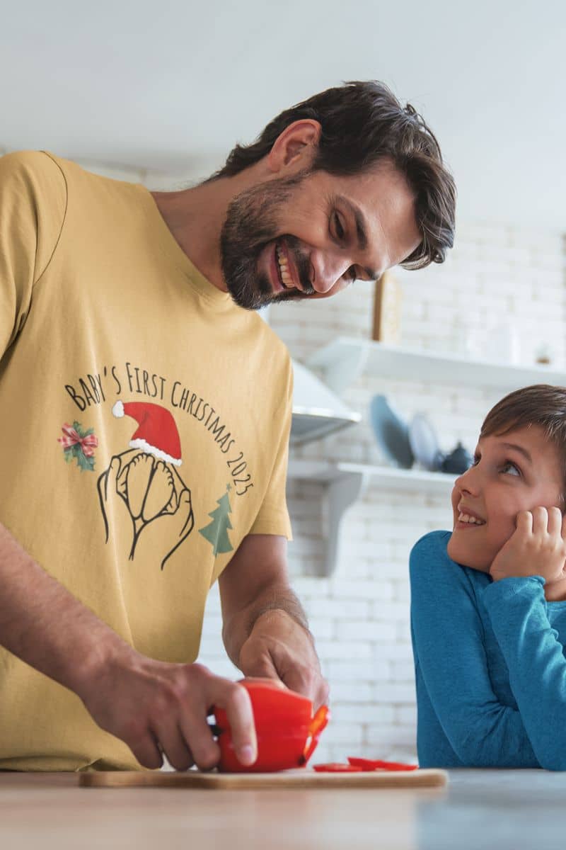 Baby's First Christmas 2025 T-Shirt with a man talking to his son while cutting bell peppers