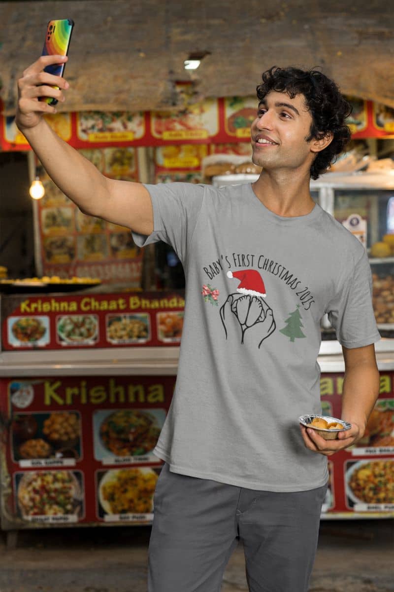 Baby's First Christmas 2025 T-Shirt with a man taking a selfie in a fast food restaurant