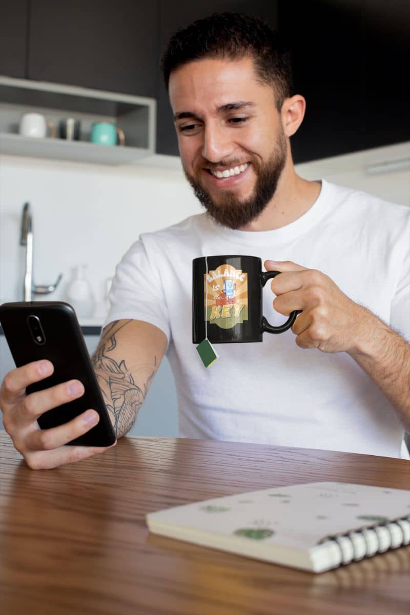Balance is the key mug with a man holding a cup of tea and looking at his phone in the kitchen