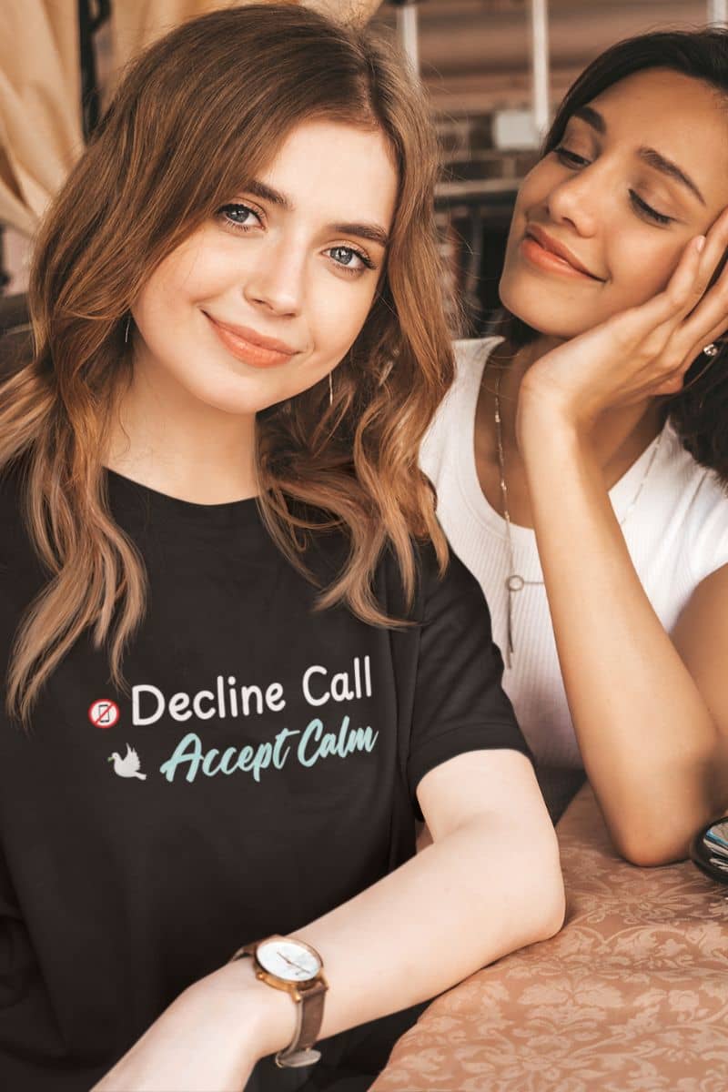 Calm quote t-shirt with two women sitting together, one wearing a black t-shirt with text 'Decline Call Accept Calm', in a casual setting.