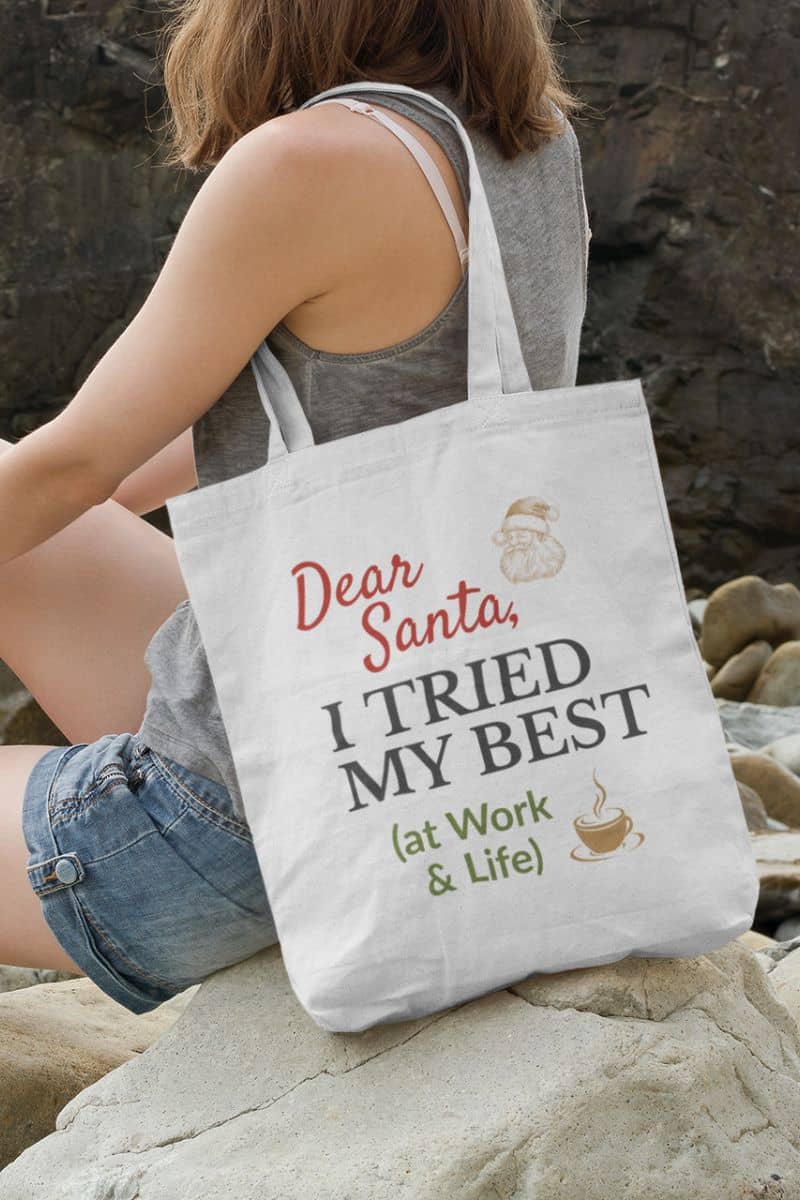 Christmas humor tote bag with a person holding a tote bag with humorous text 'Dear Santa, I tried my best (at work & life)' on rocks