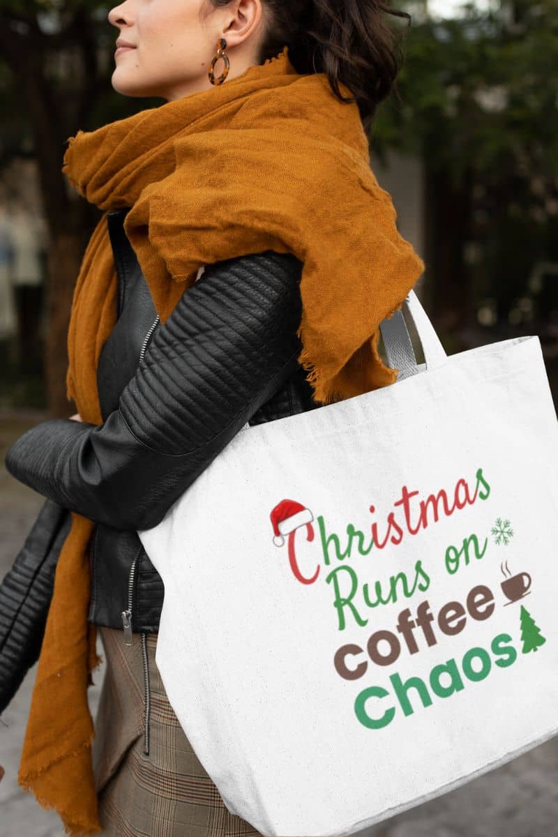 Coffee lover Christmas tote with a person wearing a mustard yellow scarf and holding a tote bag with text 'Christmas Runs on Coffee Chaos'