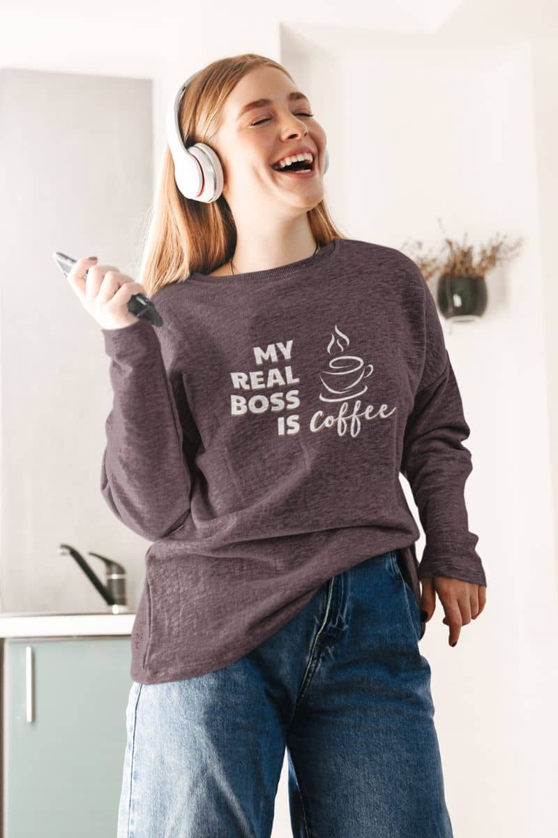 Coffee sweatshirt with a girl wearing a sweatshirt with 'My real boss is coffee' text in a kitchen.