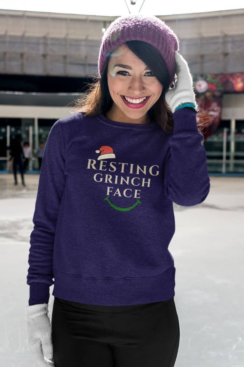 Comfy Christmas sweater with a person wearing a purple sweatshirt with 'Resting Grinch Face' text, standing outdoors.