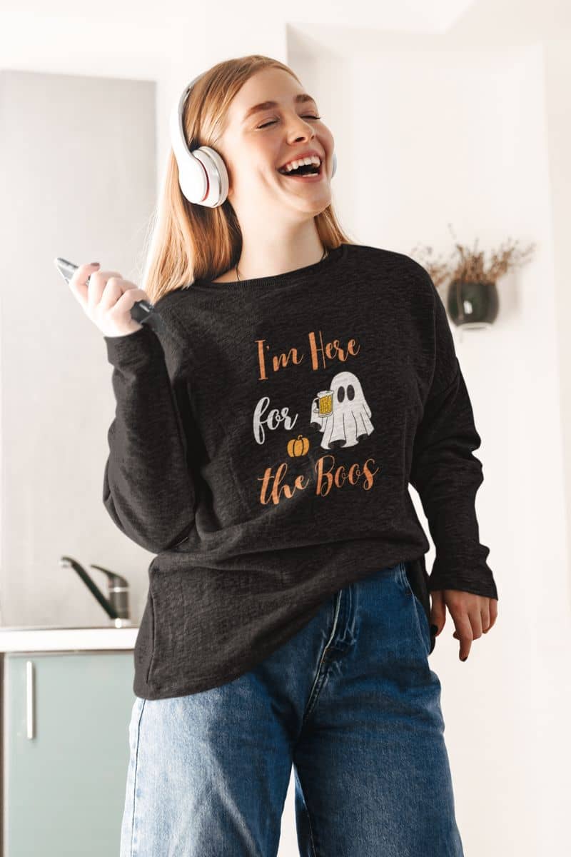 Cozy Halloween pullover with a person wearing a dark gray sweatshirt with Halloween-themed text and graphics, standing in a kitchen.