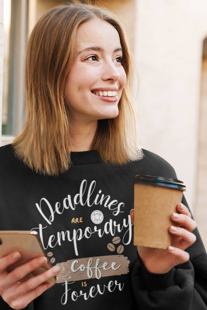 Cozy coffee enthusiast sweatshirt with a girl smiling while holding a cup of coffee and a phone in her hand