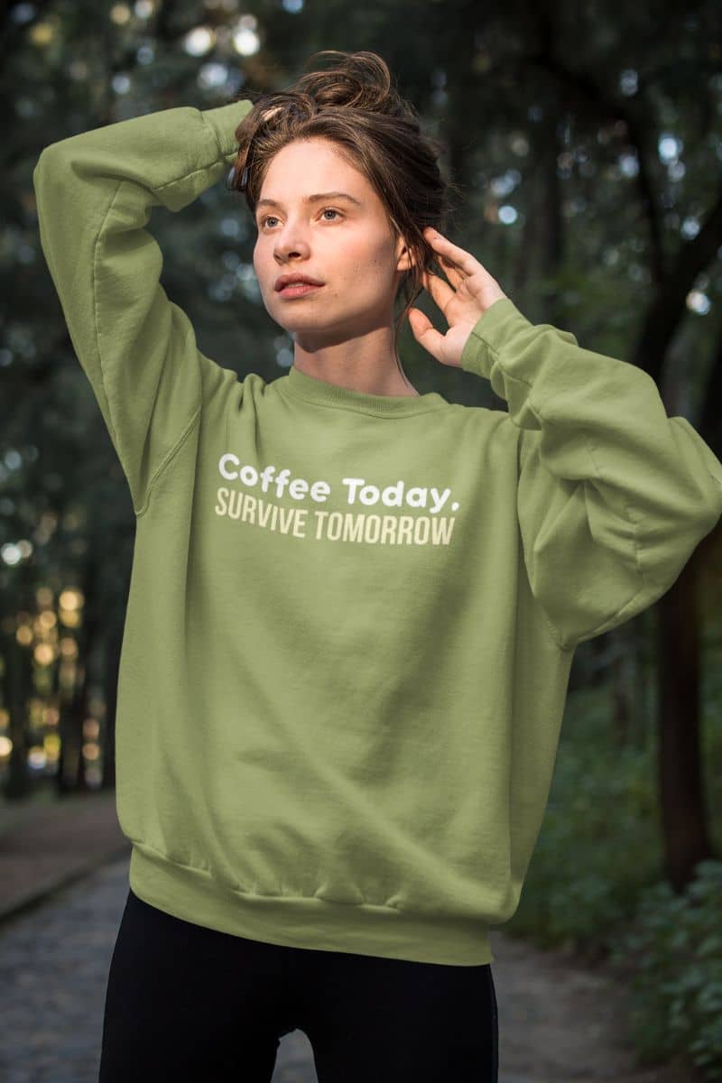 Cozy coffee pullover with a girl in a green sweatshirt with the text 'Coffee Today, Survive Tomorrow' in the woods.