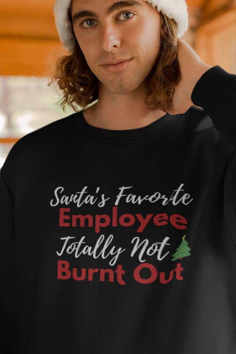 Cozy self care pullover with a person wearing a black sweatshirt with text 'Santa's Favorite Employee Totally Not Burnt Out' and a Christmas tree.