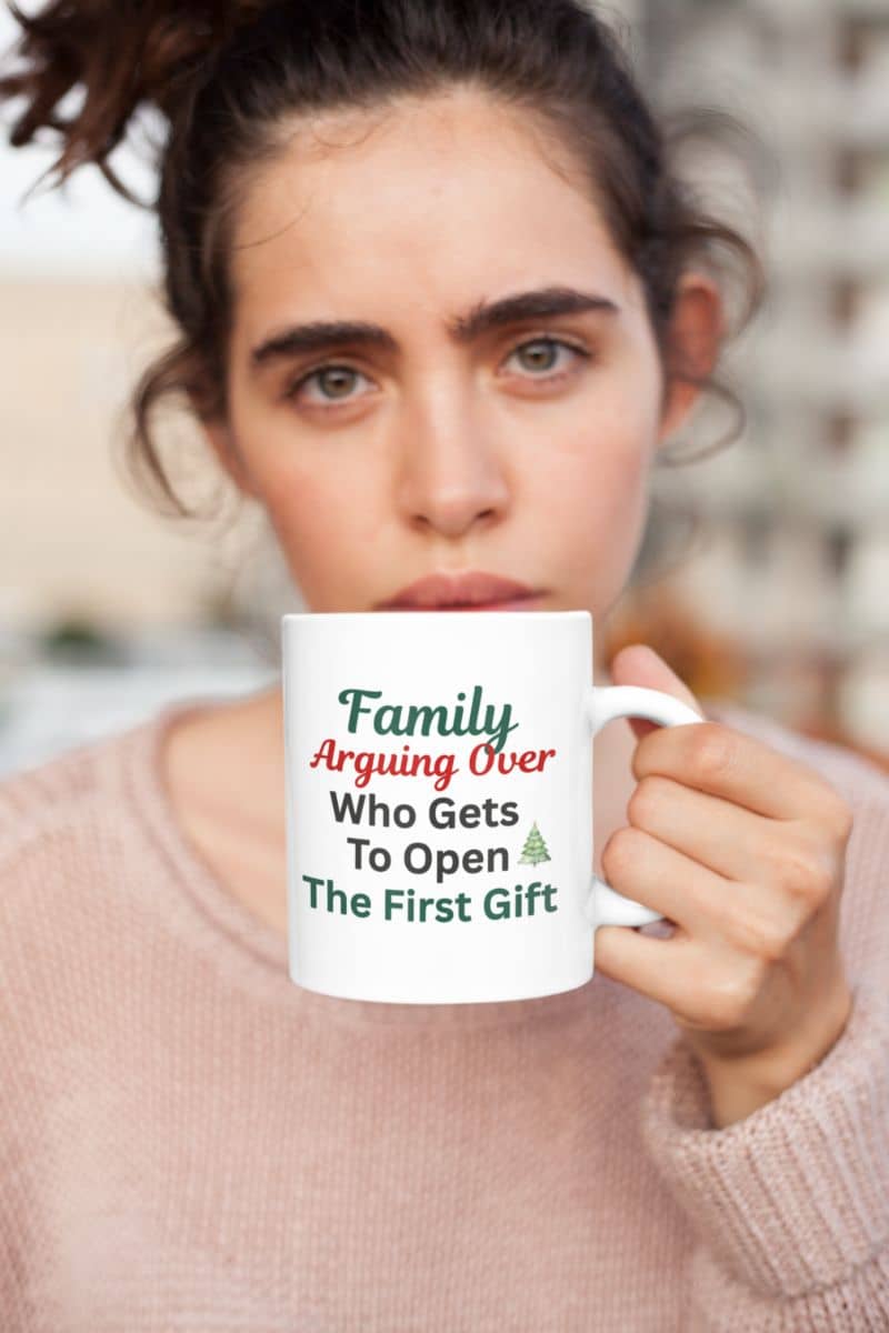 Cute family holiday mug with a person holding a mug with text 'Family Arguing Over Who Gets To Open The First Gift' against a blurred background