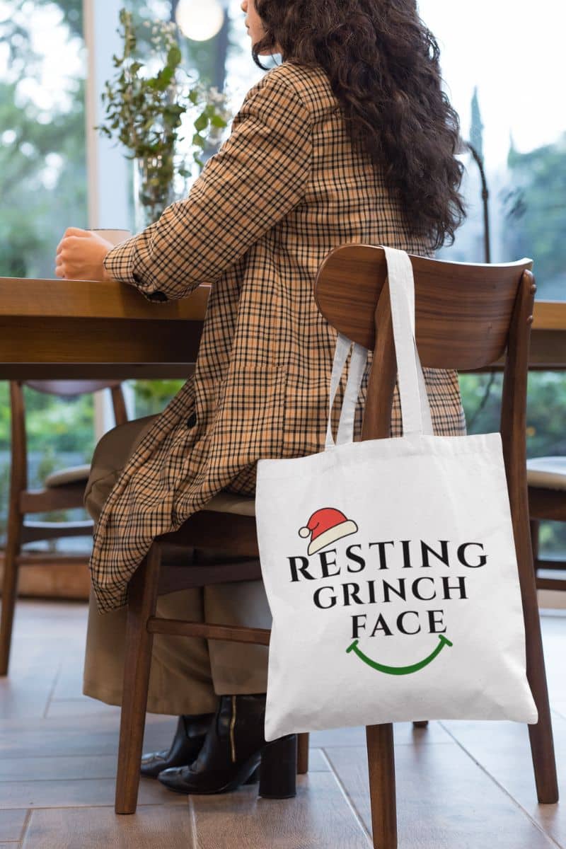 Eco friendly gift bag with a person sitting at a table with a tote bag featuring 'Resting Grinch Face' text.