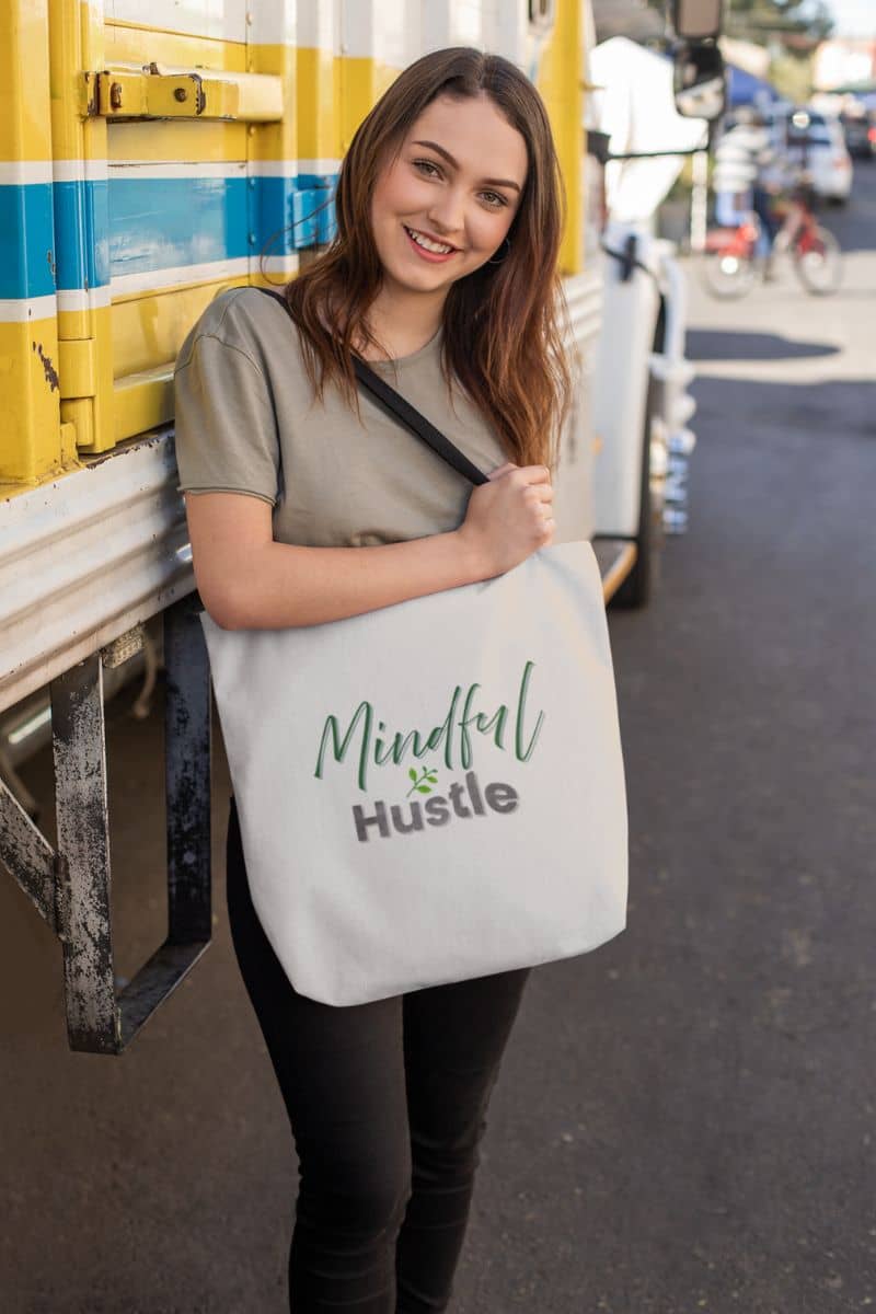 Empowerment message tote with a woman holding a tote bag with 'Mindful Hustle' text, standing next to a yellow truck.