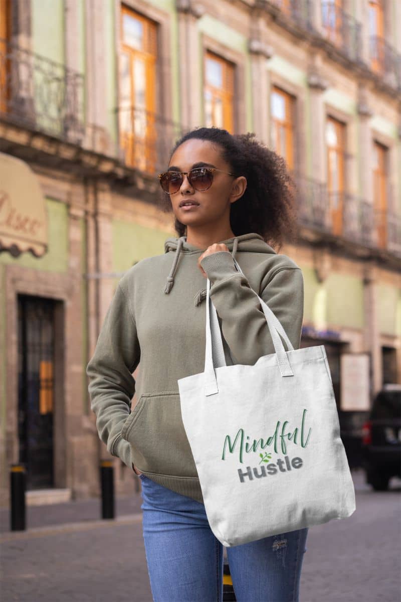 Everyday hustle tote with a woman holding a tote bag with 'Mindful Hustle' text on a city street.