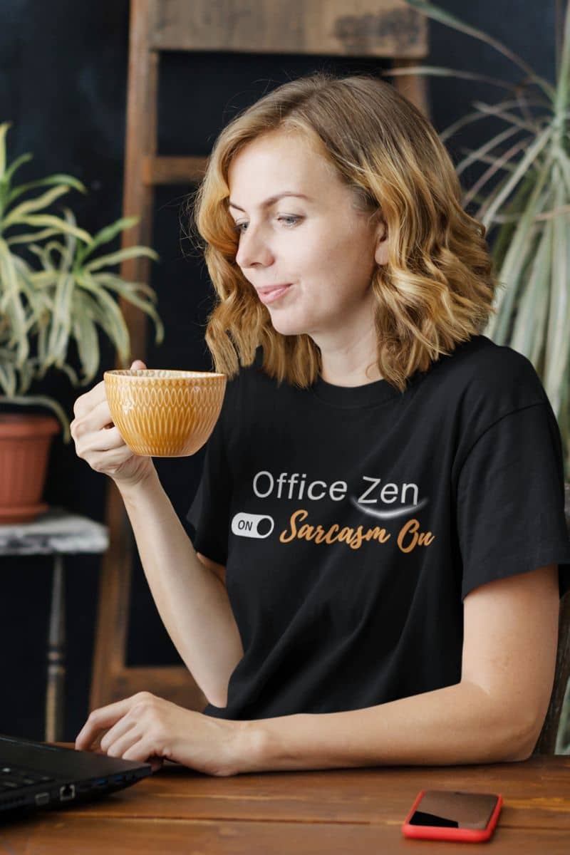 Everyday wear t-shirt with a woman wearing a black t-shirt with 'Office Zen' text, holding a mug and using a laptop.