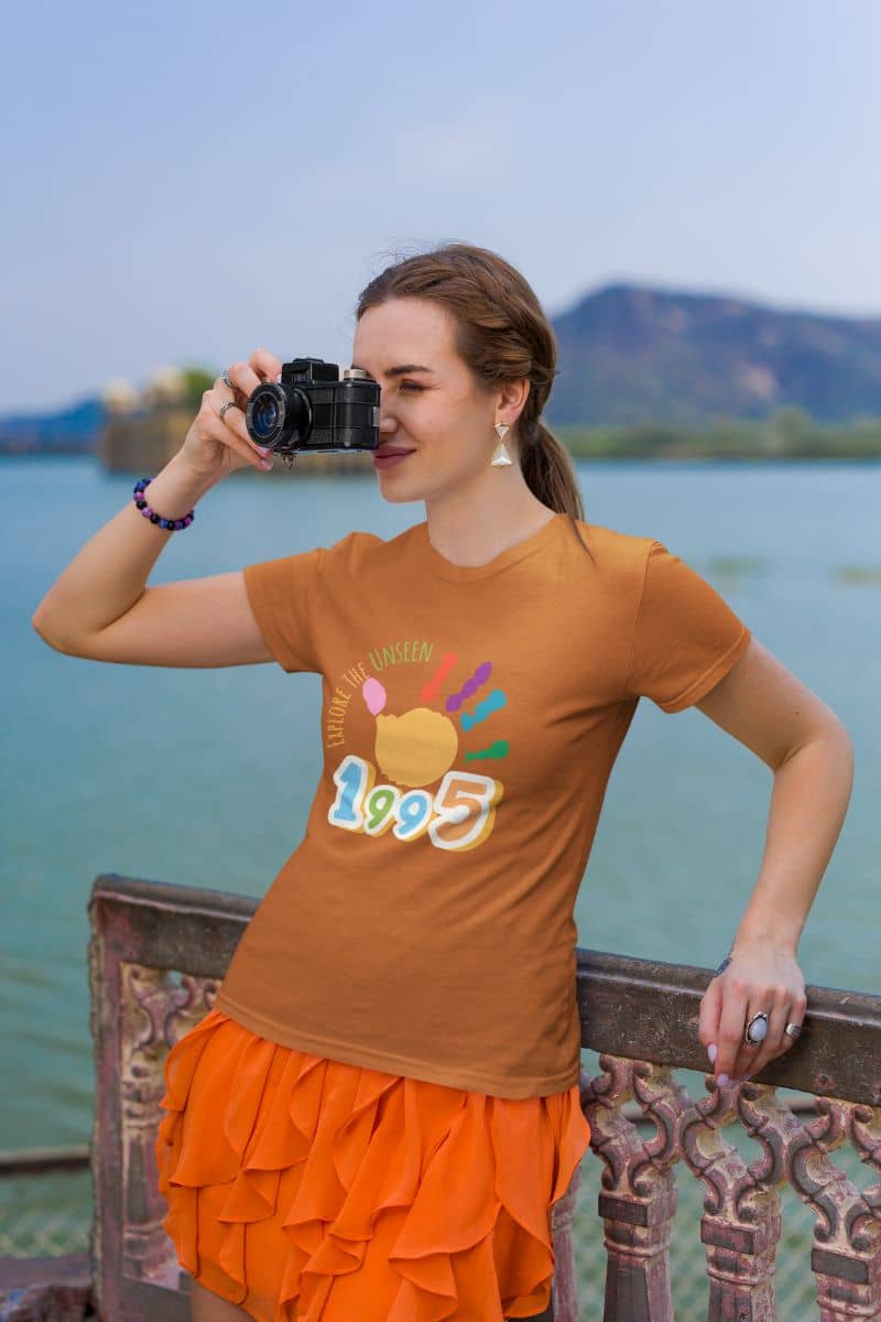 Explore the unseen t-shirt with the girl standing taking pictures at the beach's bridge railing