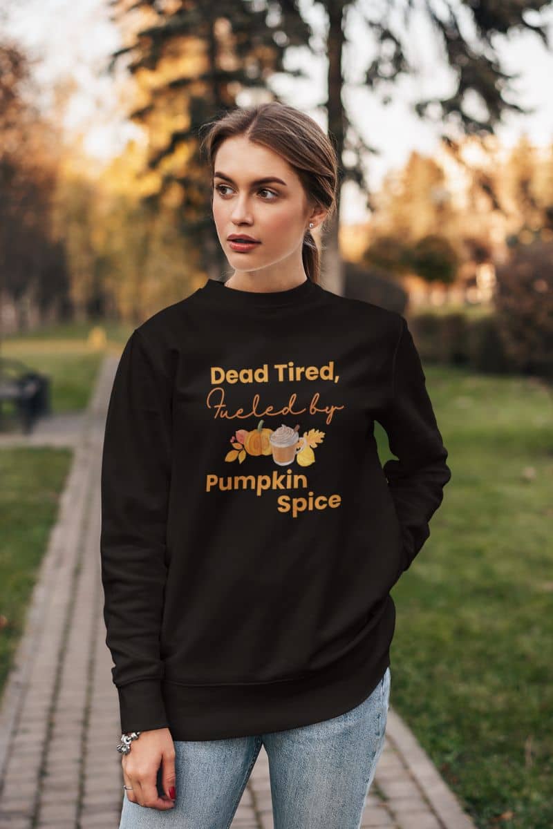 Fall coffee sweatshirt with a woman wearing a black sweatshirt with text 'Dead Tired, Fueled by Pumpkin Spice' in an outdoor setting