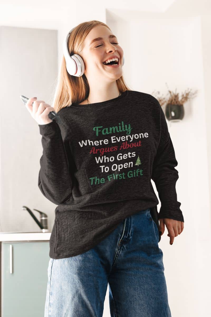 Family humor holiday sweater with a person wearing a sweater with a humorous family quote 'Family: Where Everyone Argues About Who Gets To Open The First Gift', standing in a kitchen.