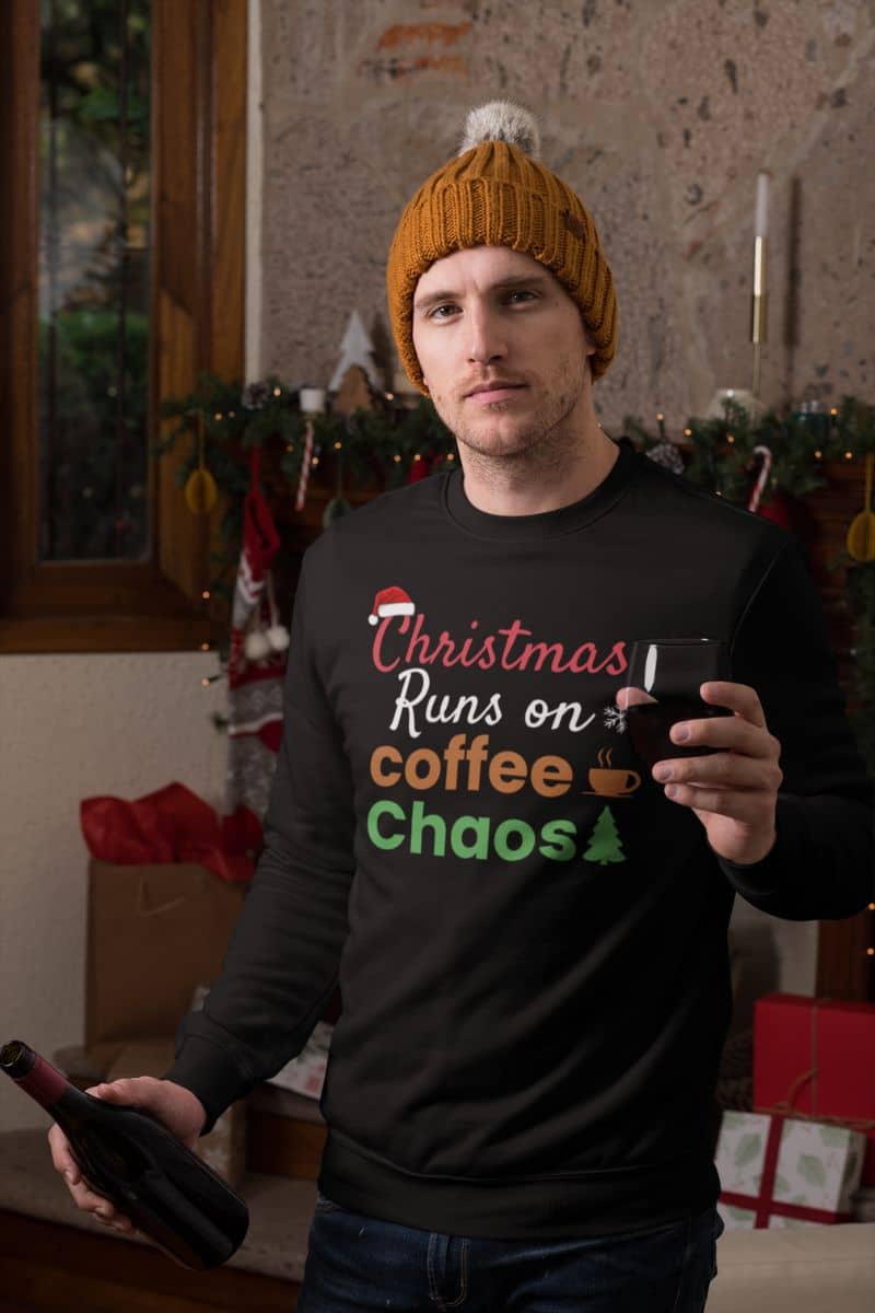 Festive holiday crewneck with a man wearing a black sweater with text 'Christmas Runs on Coffee & Chaos', holding a bottle, in a festive indoor setting.