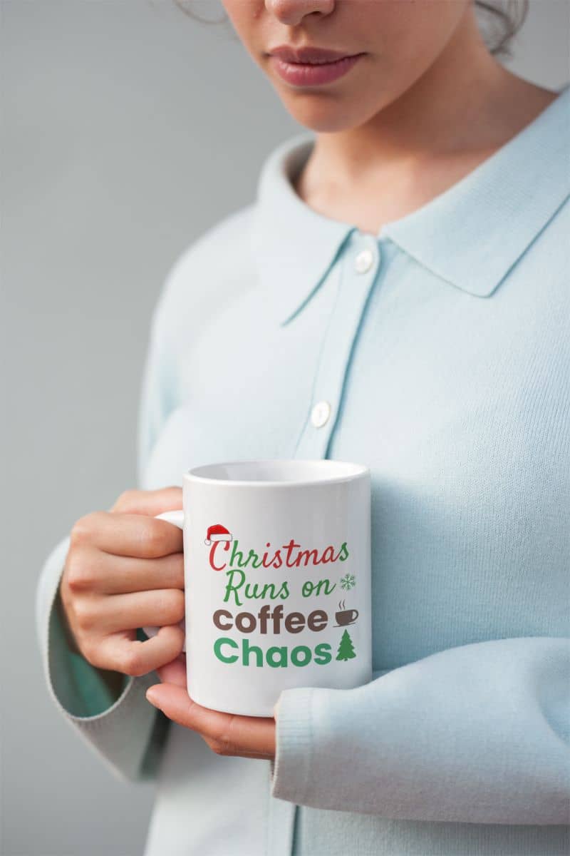 Funny Christmas mug with a person holding a mug with 'Christmas Runs on Coffee Chaos' text