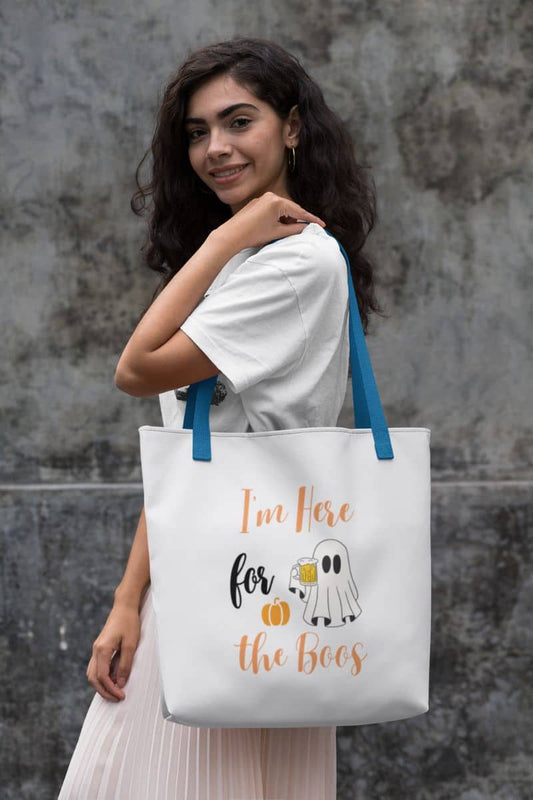 Funny Halloween tote bag displaying a woman holding a tote bag with text 'I’m Here for the Boos' against a textured wall.