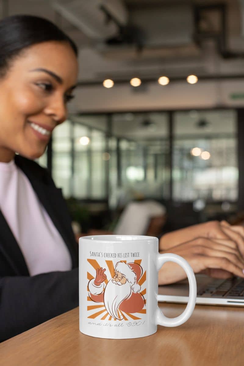 Funny Santa Mug - Santa's Checked His List Twice And It's All OK with a woman working next to a cup of coffee