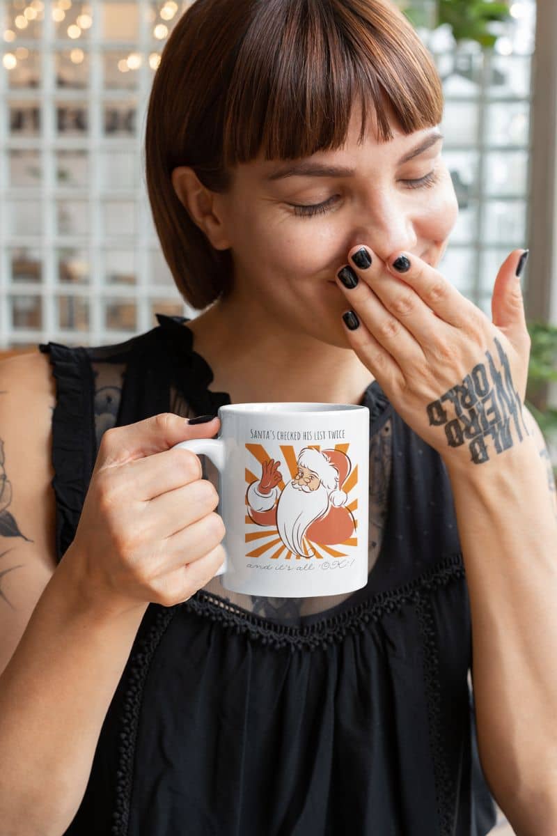 Funny Santa Mug - Santa's Checked His List Twice And It's All OK with a woman covering her mouth laughing with tattoos on her arms