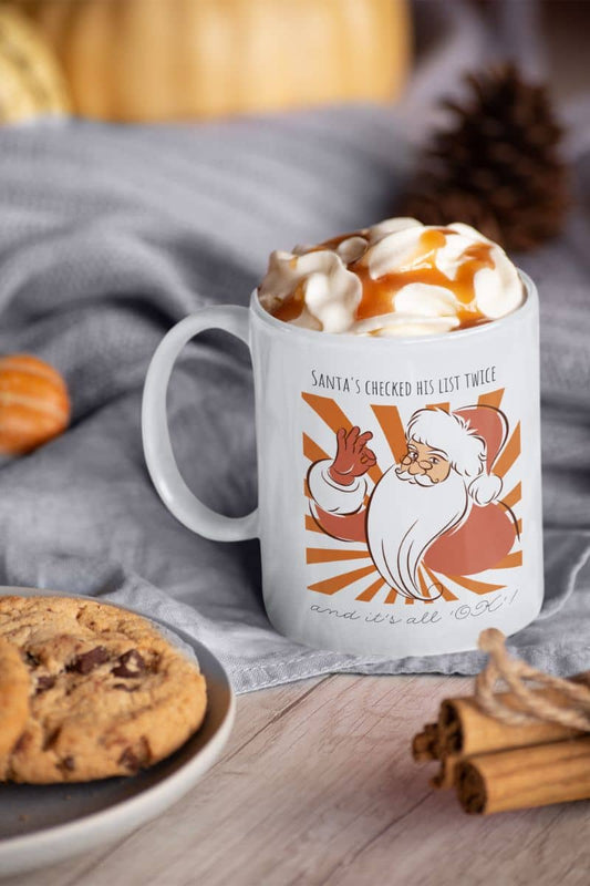 Funny Santa Mug - Santa's Checked His List Twice And It's All OK with a cup of coffee and a plate of cookies on the table