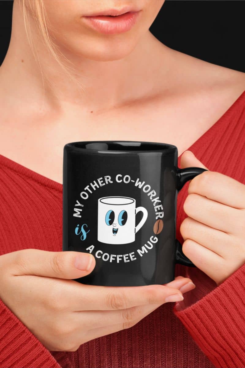 Funny coffee mugs with a girl wearing a red long sleeve off shoulder t-shirt holding a black mug that reads My Other Co-Worker is a Coffee Mug