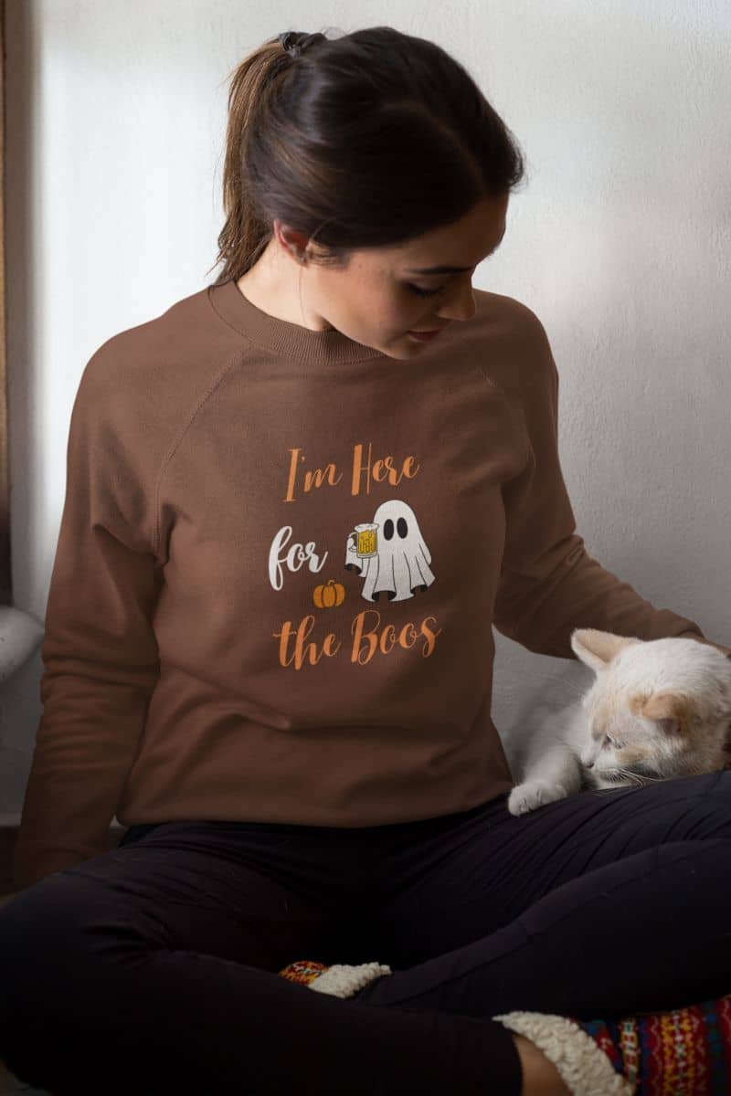 Funny fall sweatshirt with a person wearing a brown sweatshirt with a ghost and pumpkin design, sitting with a cat.