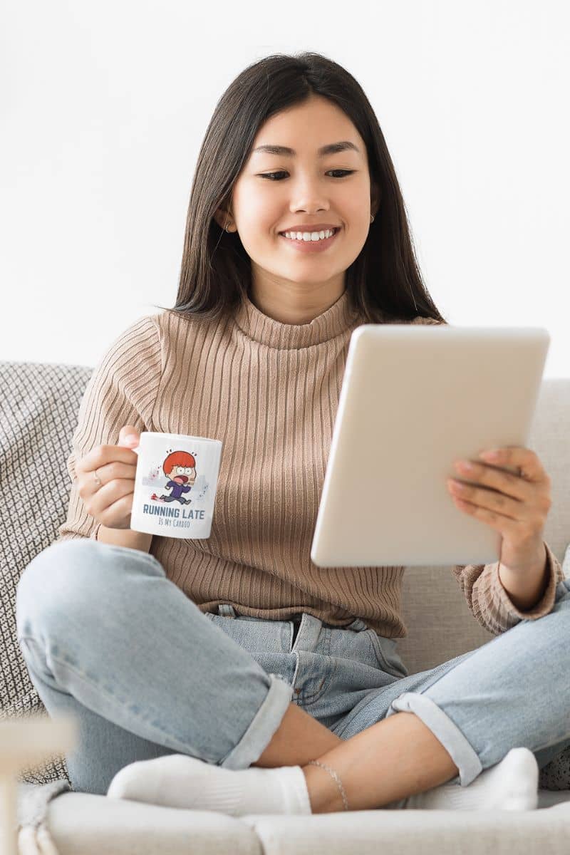 Funny running mug with a girl sitting cross-legged on the sofa and smiling while looking at her tablet