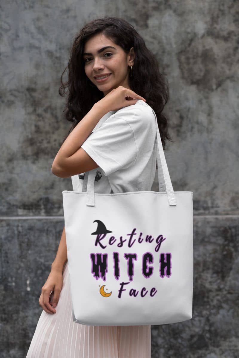 Funny witch tote with a woman holding a tote bag with 'Resting Witch Face' text against a gray wall.