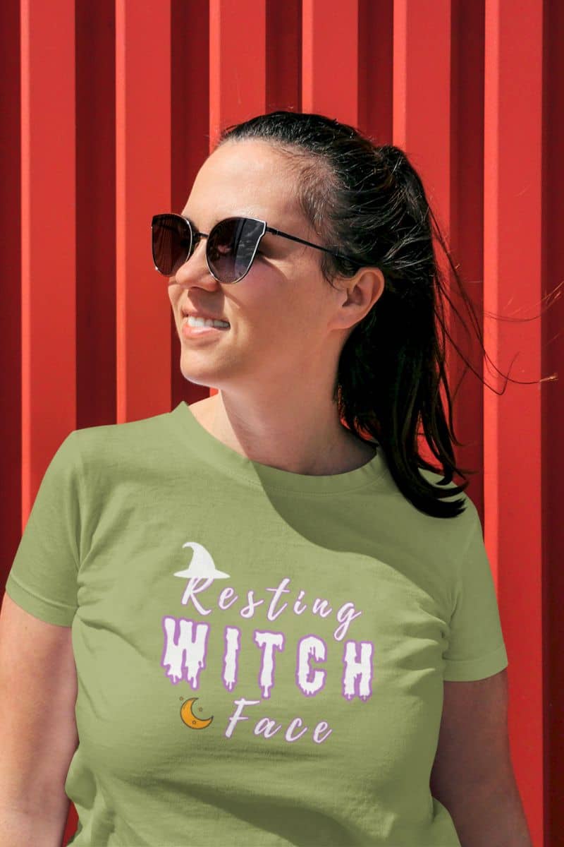 Halloween witch shirt with a woman displaying a green t-shirt with 'Resting Witch Face' text against a red background