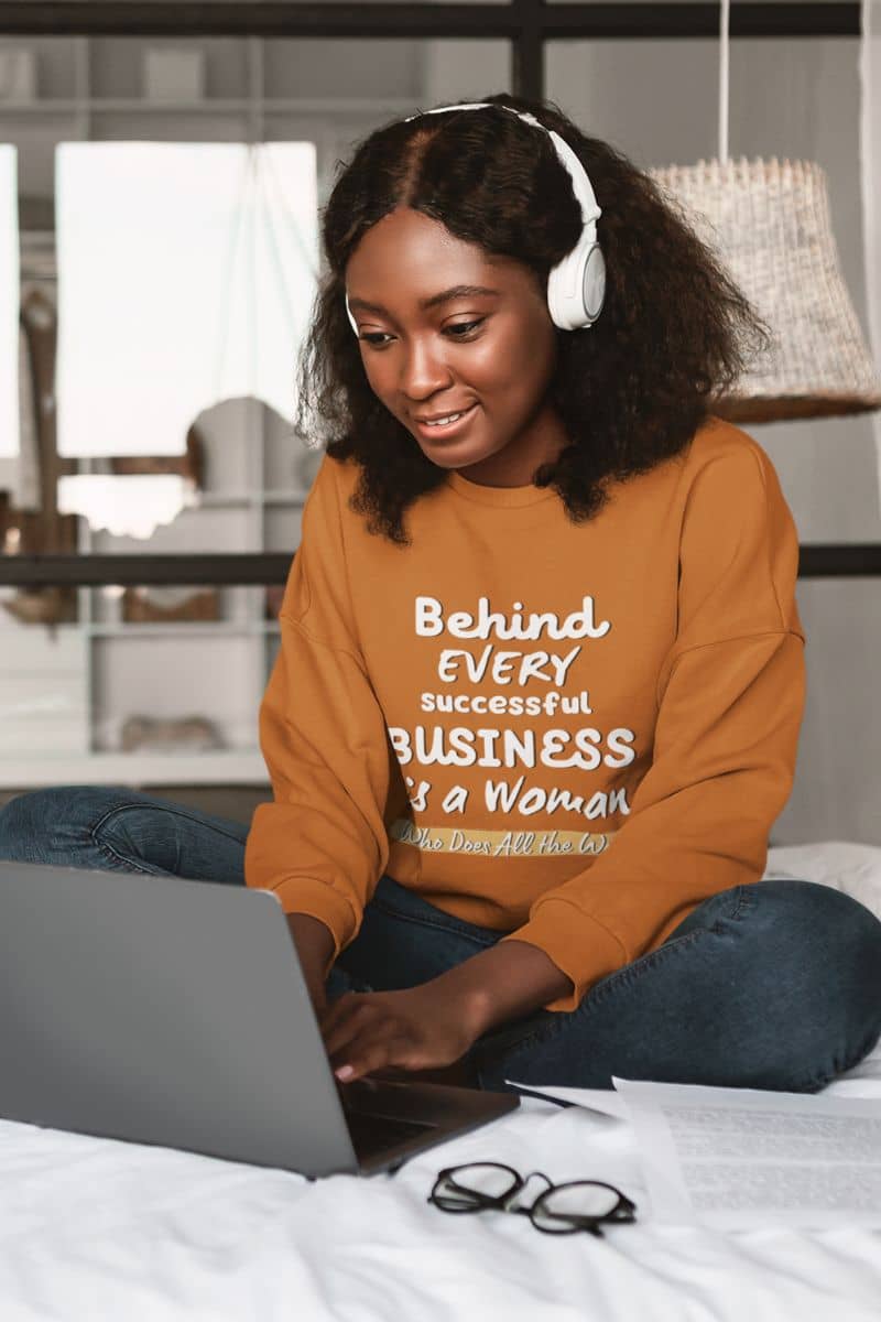 Inspirational sweatshirts with with a woman wearing headphones and working on her laptop in bed