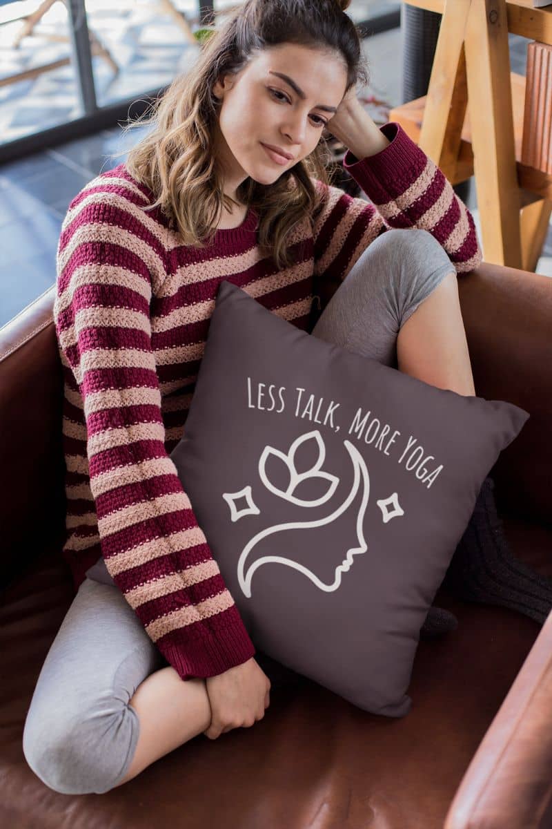 Experience Serenity with the Less Talk More Yoga Pillow with the girl hugging a pillow sitting pensively on the sofa