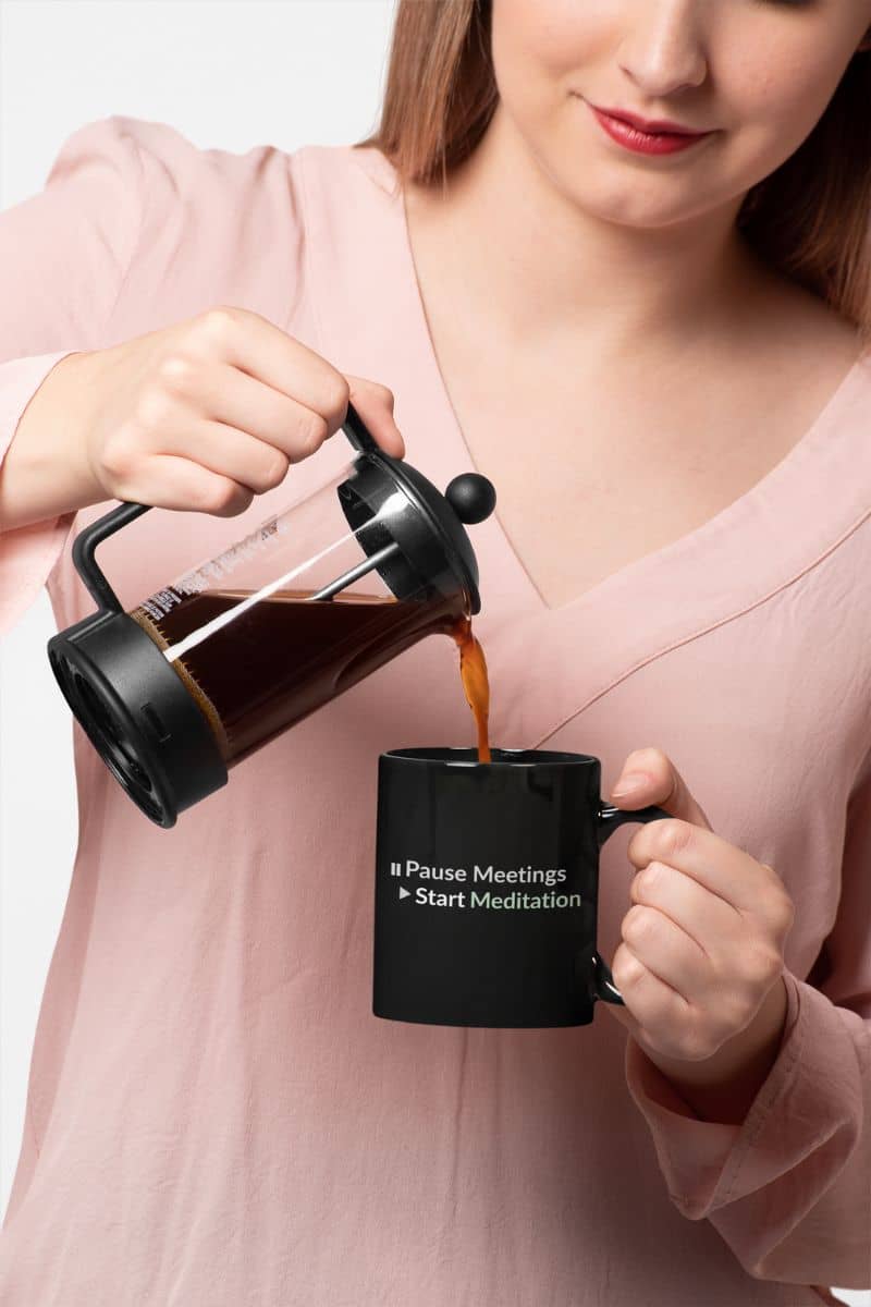 Meditation mug for office with a person pouring coffee from a French press into a black mug with text.