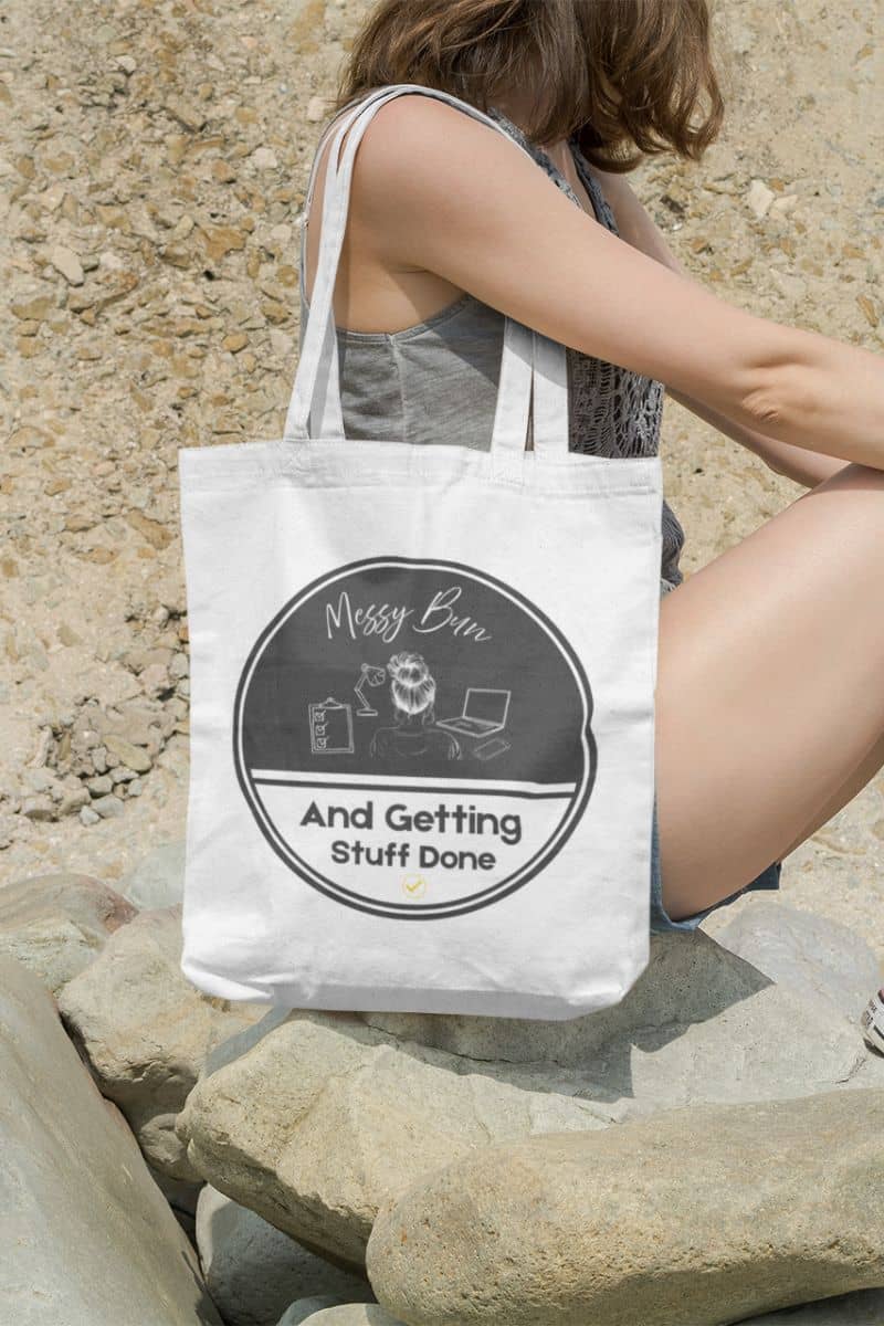 Messy bun tote bag with the girl sitting on a rock by the beach with a bag on her shoulder