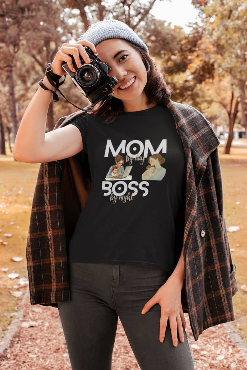 Minimalist typography t-shirt with a person wearing a black t-shirt with 'MOM by day, BOSS by night' text in an outdoor setting.