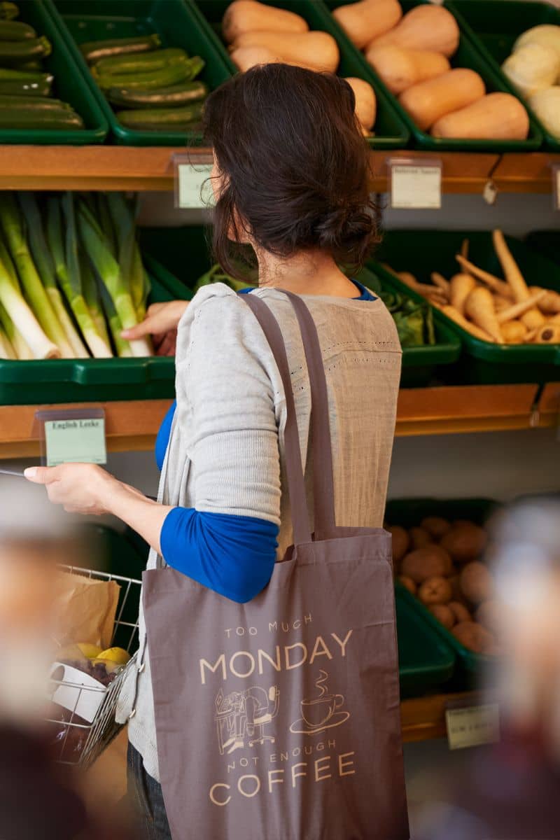 Monday mood tote with a woman carrying a tote bag choosing vegetables in a store