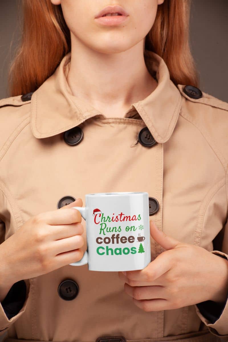 Office holiday mug with a person holding a mug with text 'Christmas runs on coffee and chaos' in a beige coat.