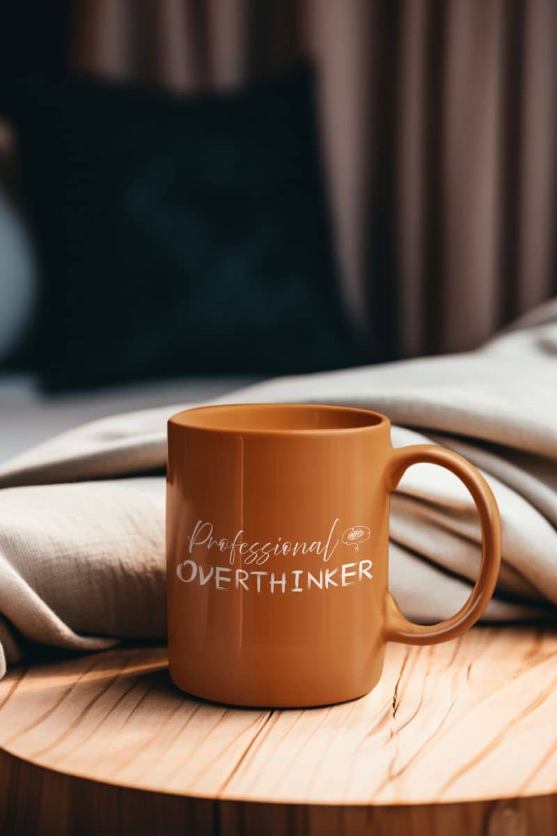 Overthinker mug with an orange coffee cup on the table in the bedroom