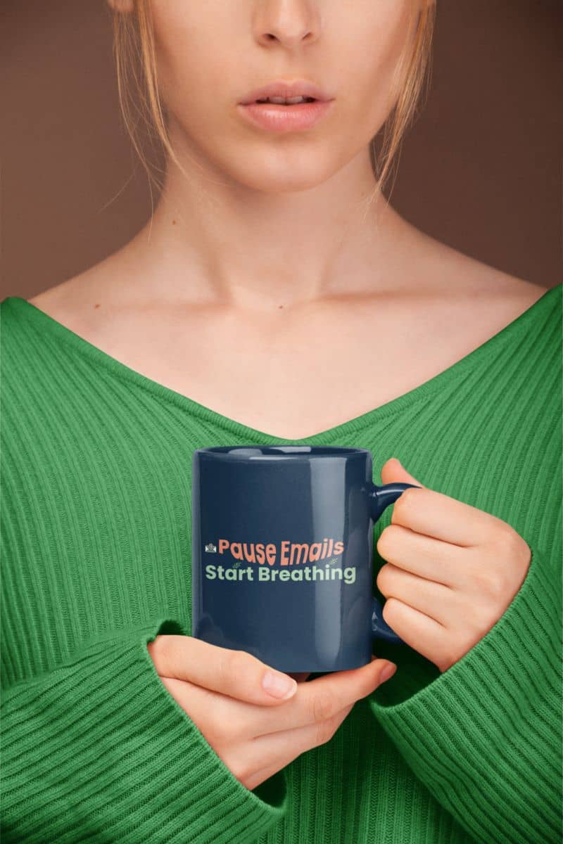 Peaceful coworker gift mug with a person holding a blue mug with text "Pause emails, Start Breathing", wearing a green sweater against a brown background