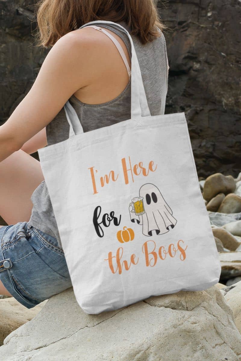 Pumpkin Halloween tote with a person holding a tote bag with Halloween design sitting on rocks.