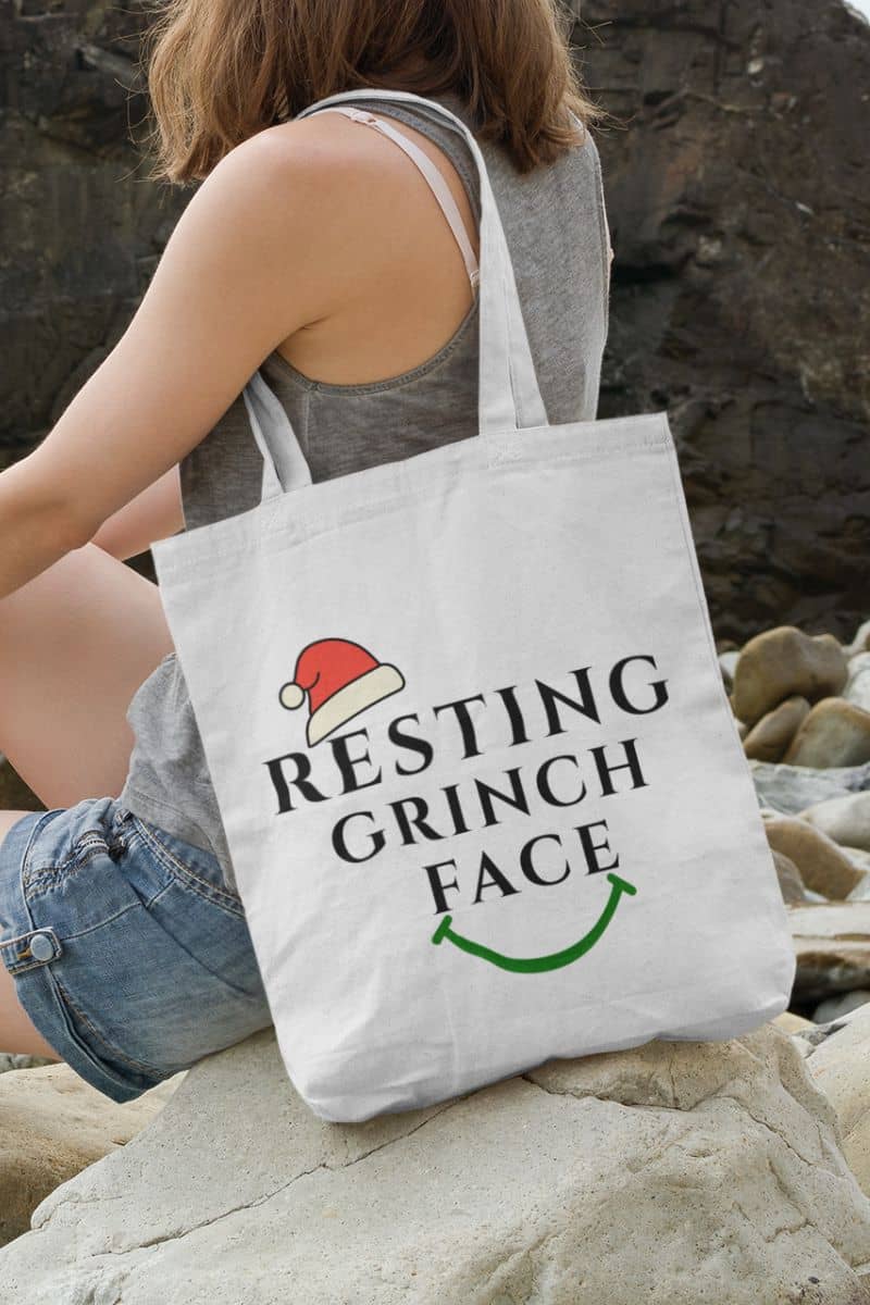 Reusable Christmas shopper with a person holding a tote bag with 'Resting Grinch Face' text on a rocky surface